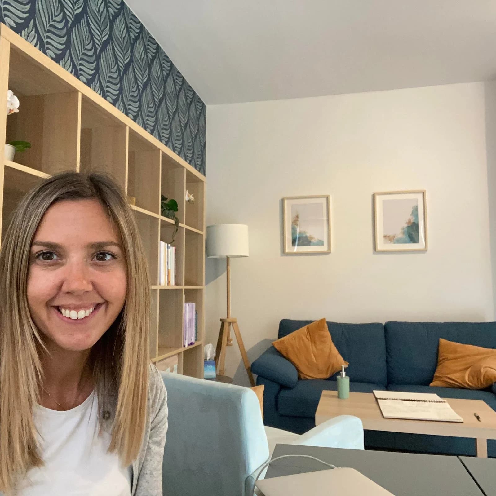 Bright mental health therapy room in Attard, Malta with a beige sofa, wooden table, and sunlit potted olive tree.